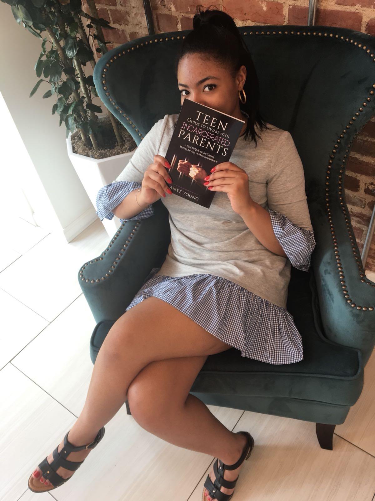 Anyé Young seated in a green armchair holding her book Teen Guide to Living With Incarcerated Parents